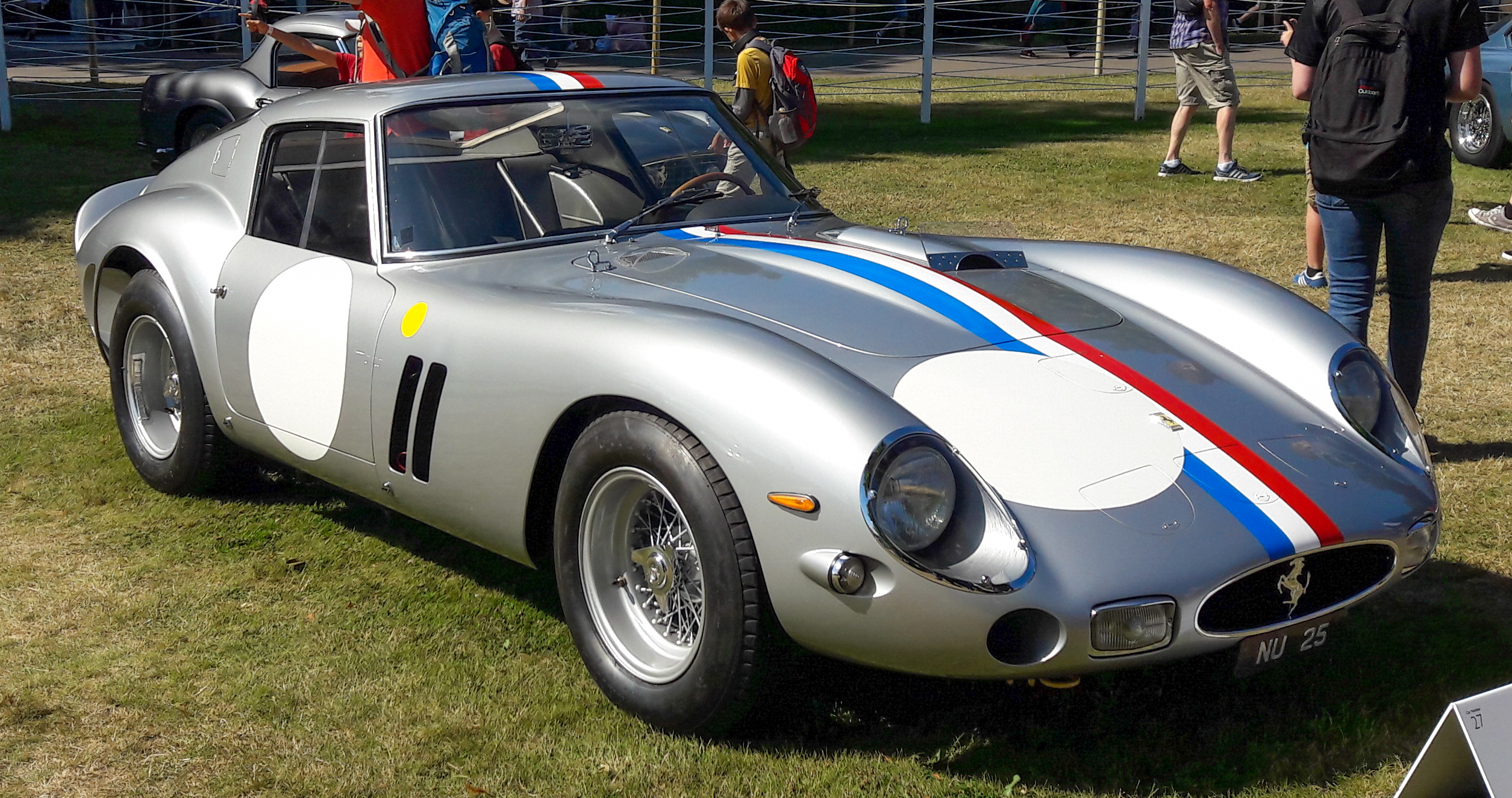 1962 Ferrari 250 GTO in Rosso Corsa parked at a historic racetrack, sculpted nose and triple vents